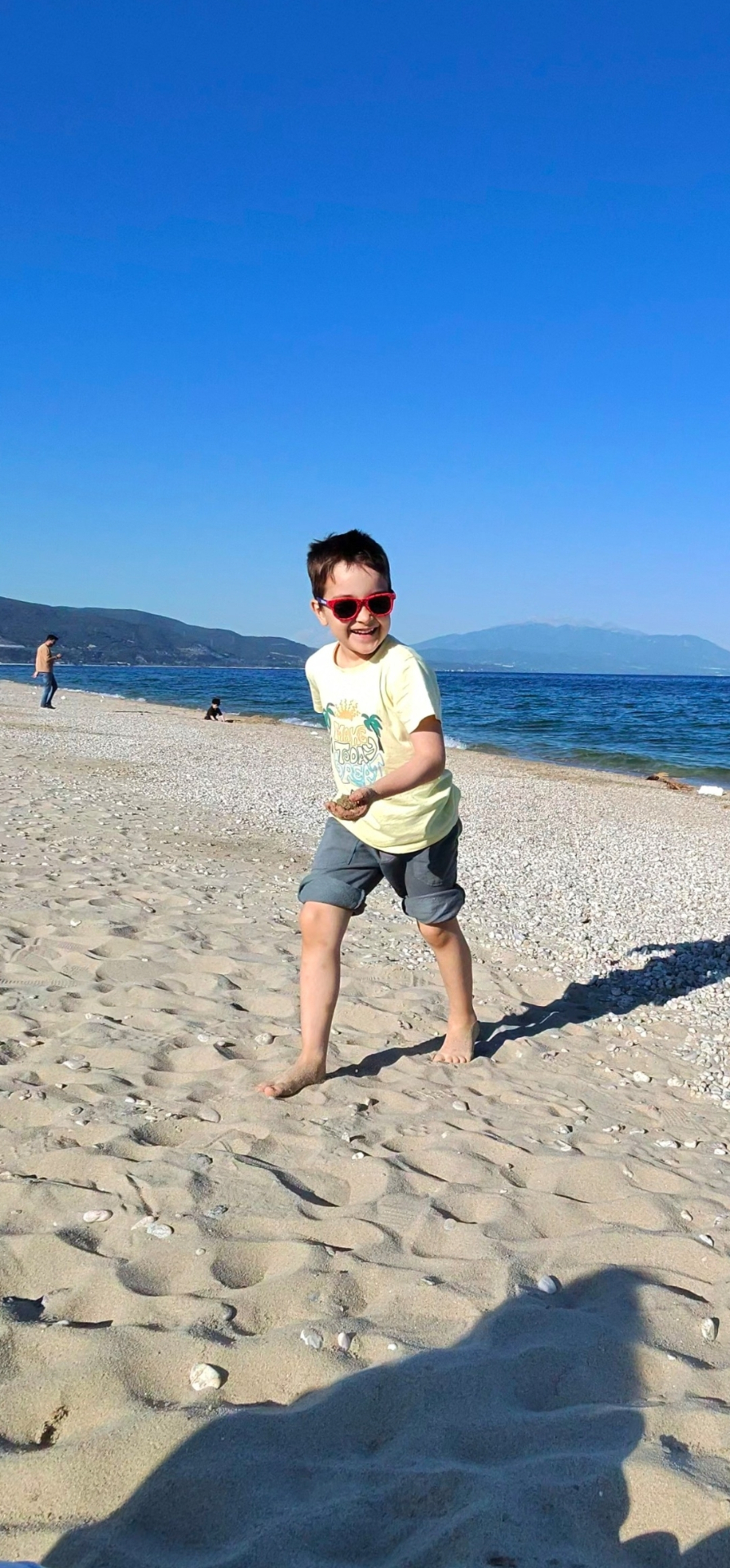 Aris smiling on the beach with red sunglasses